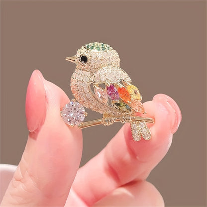 Decorative bird brooch with gemstones held between fingers against a brown background