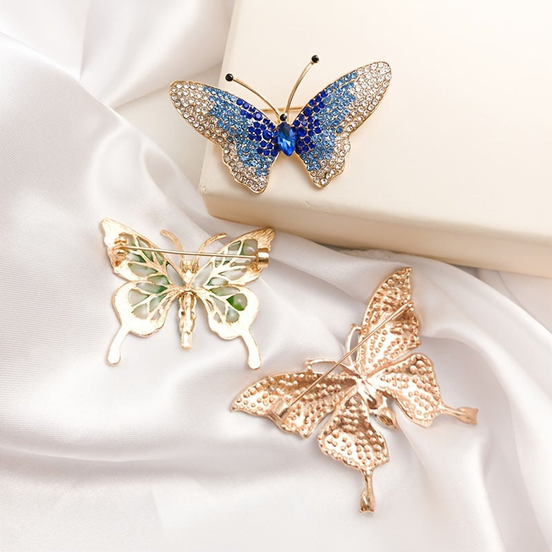 Three butterfly-shaped brooches in gold, blue, and rose gold on a white fabric background.