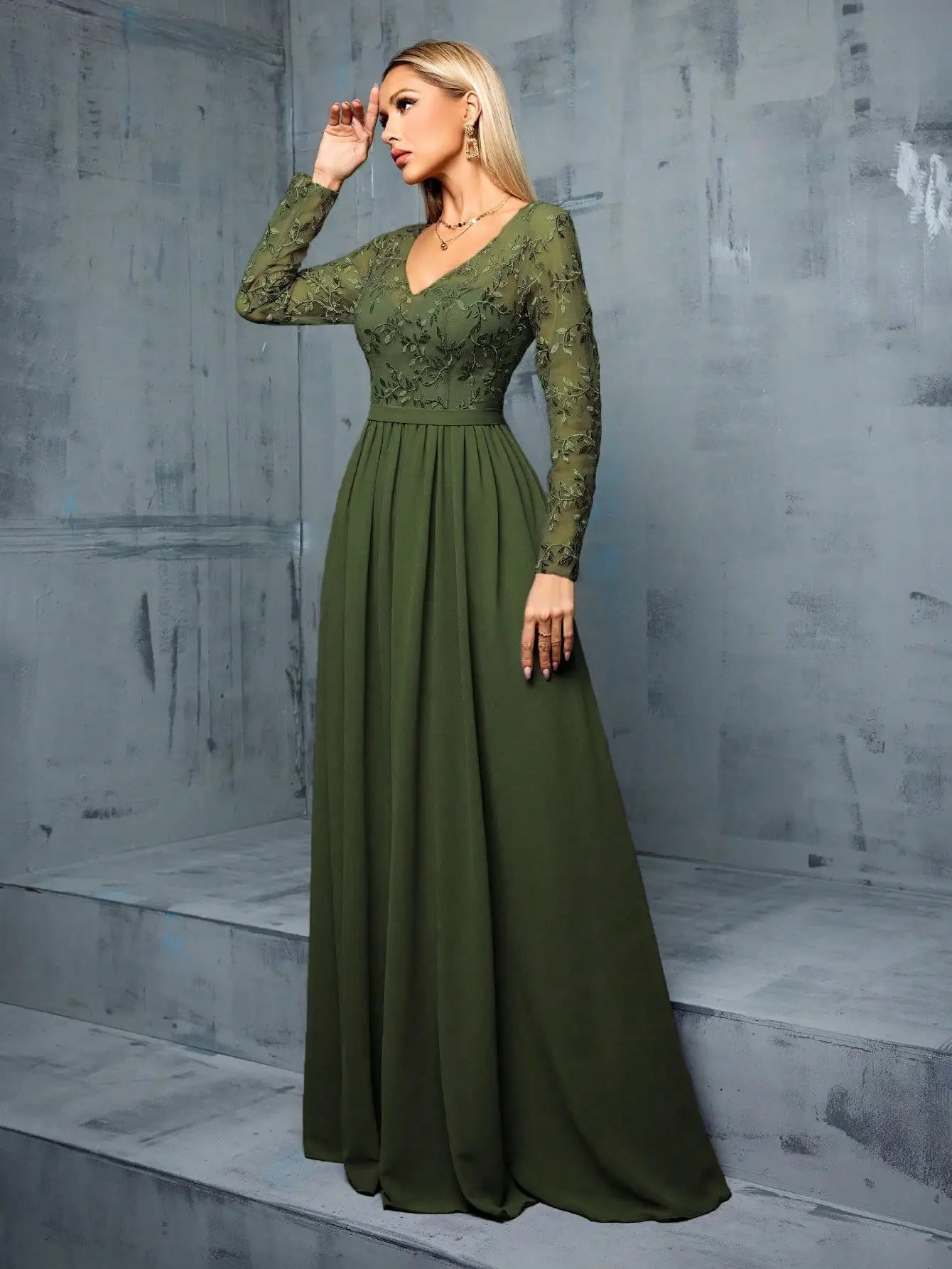 Woman wearing a green evening gown against a gray concrete wall.