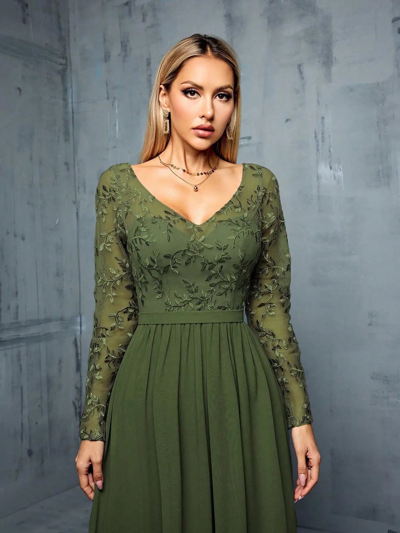 Woman wearing a green lace dress against a gray concrete wall