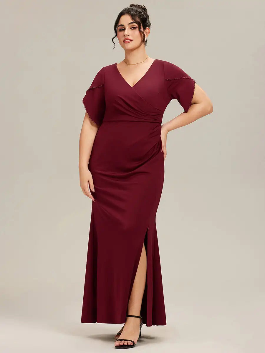Woman wearing a burgundy evening gown with a slit on a plain background