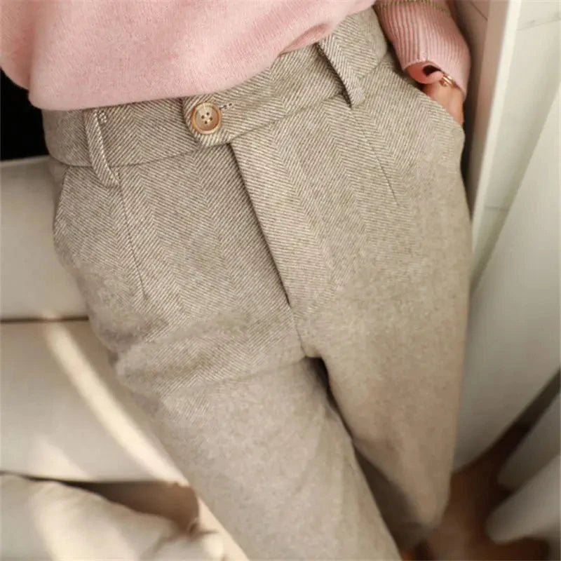 Close-up of beige pants with a button, worn by a person sitting on a white surface.