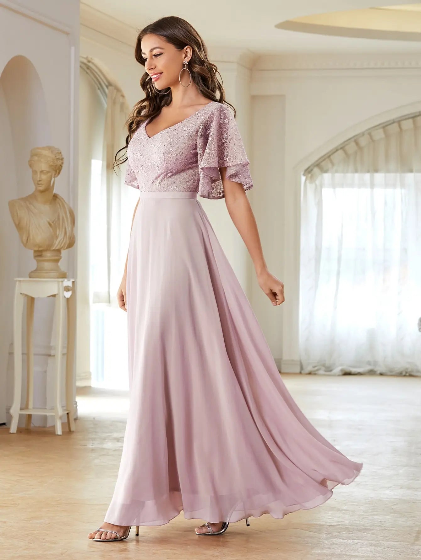 Woman in a pink dress standing in a well-lit room with a classical statue in the background.