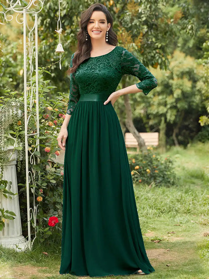 Woman wearing a green dress standing outdoors with greenery in the background