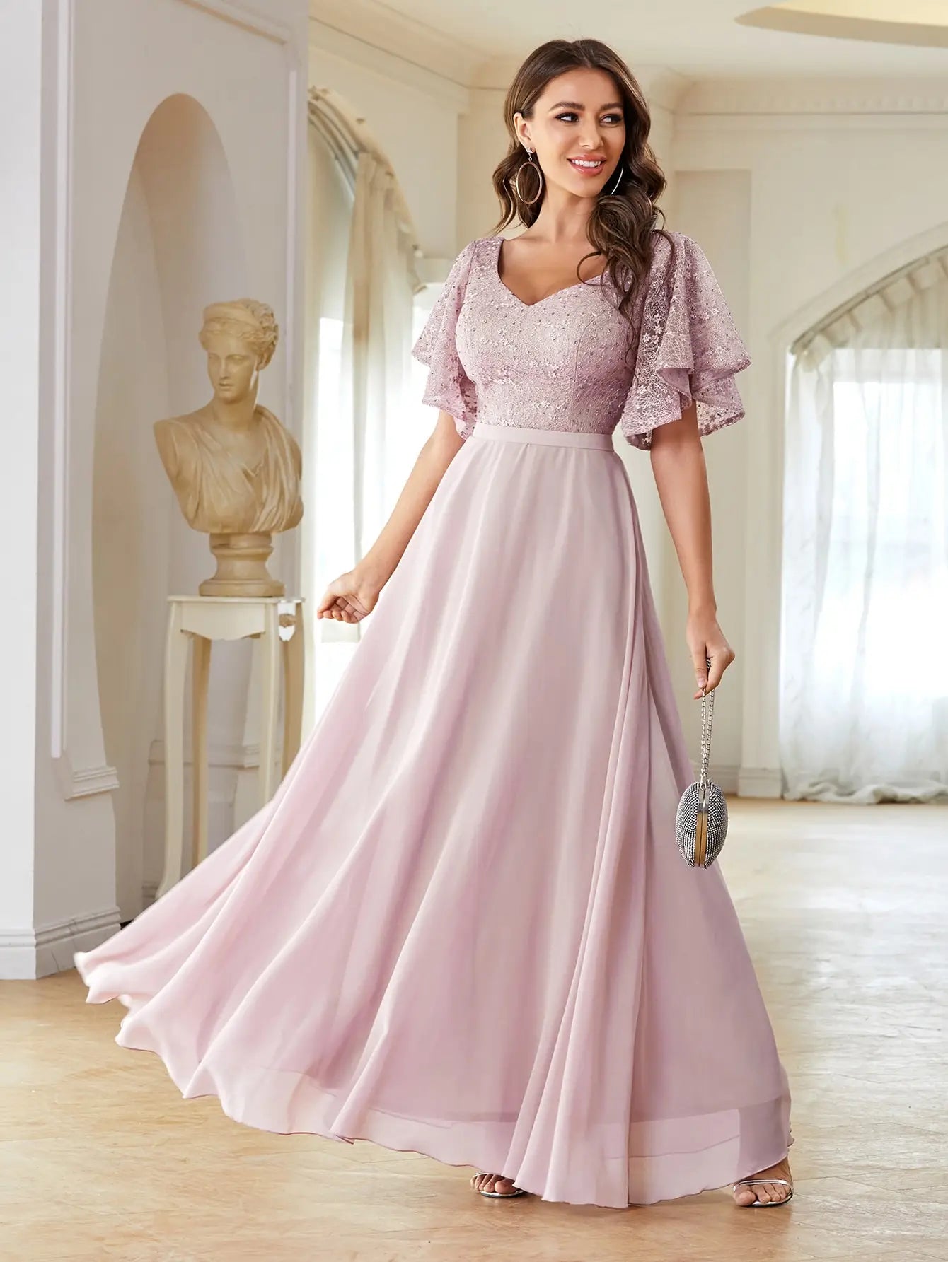 Woman wearing a pink dress in an elegant room with a statue and window.