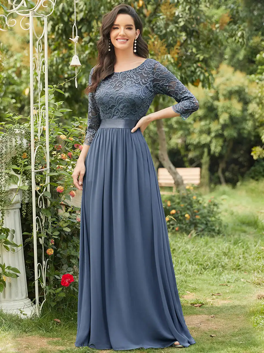 Woman wearing a long blue dress with lace detailing in an outdoor setting.