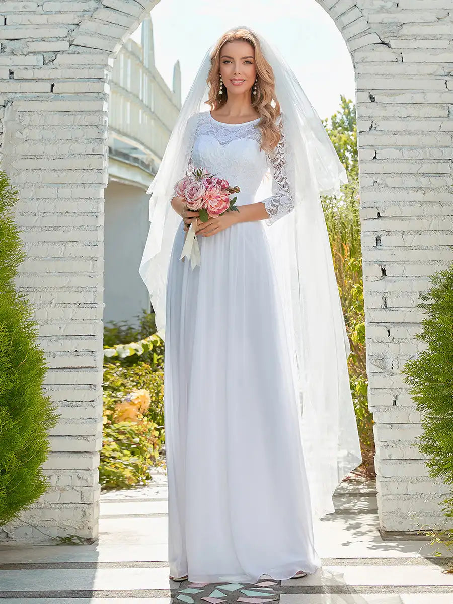 Woman in a white wedding dress holding flowers, standing in front of a stone archway.