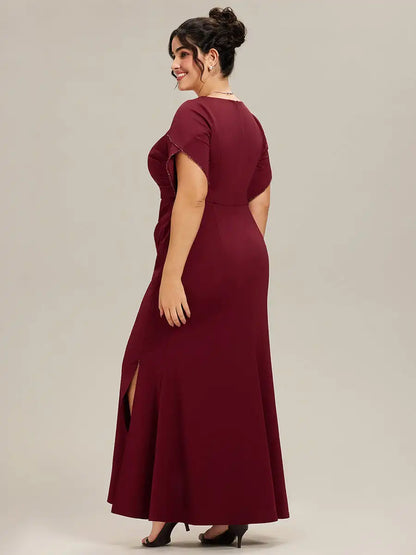 Woman wearing a burgundy evening gown with a slit on a plain background