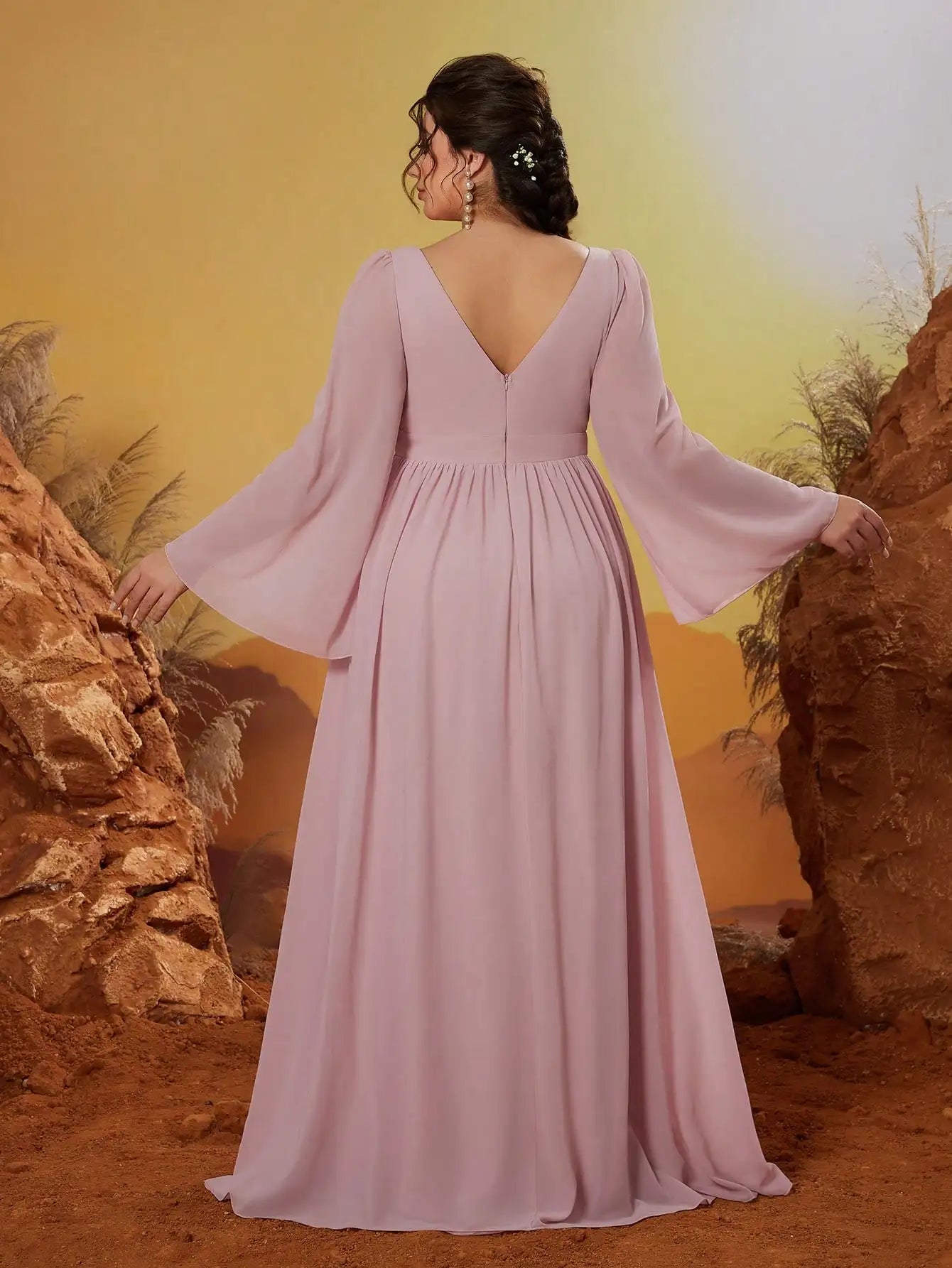 Woman in a long, light pink dress with bell sleeves standing in a desert landscape.