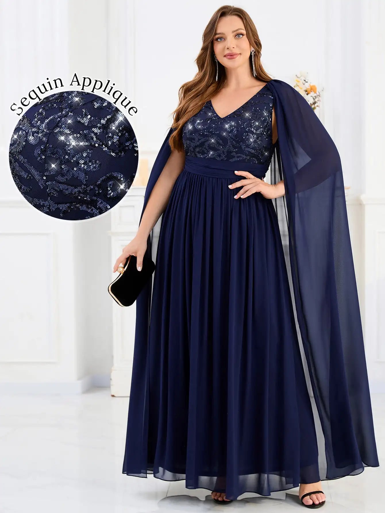 Woman wearing a navy blue evening gown with sequin applique and cape, on a white background.