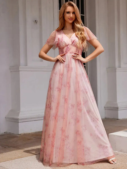 Woman wearing a pink floral dress standing in an elegant interior setting.