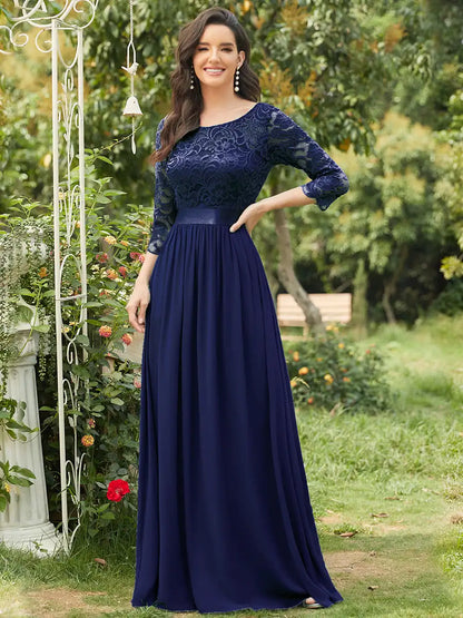 Woman in a navy blue dress standing outdoors with greenery in the background