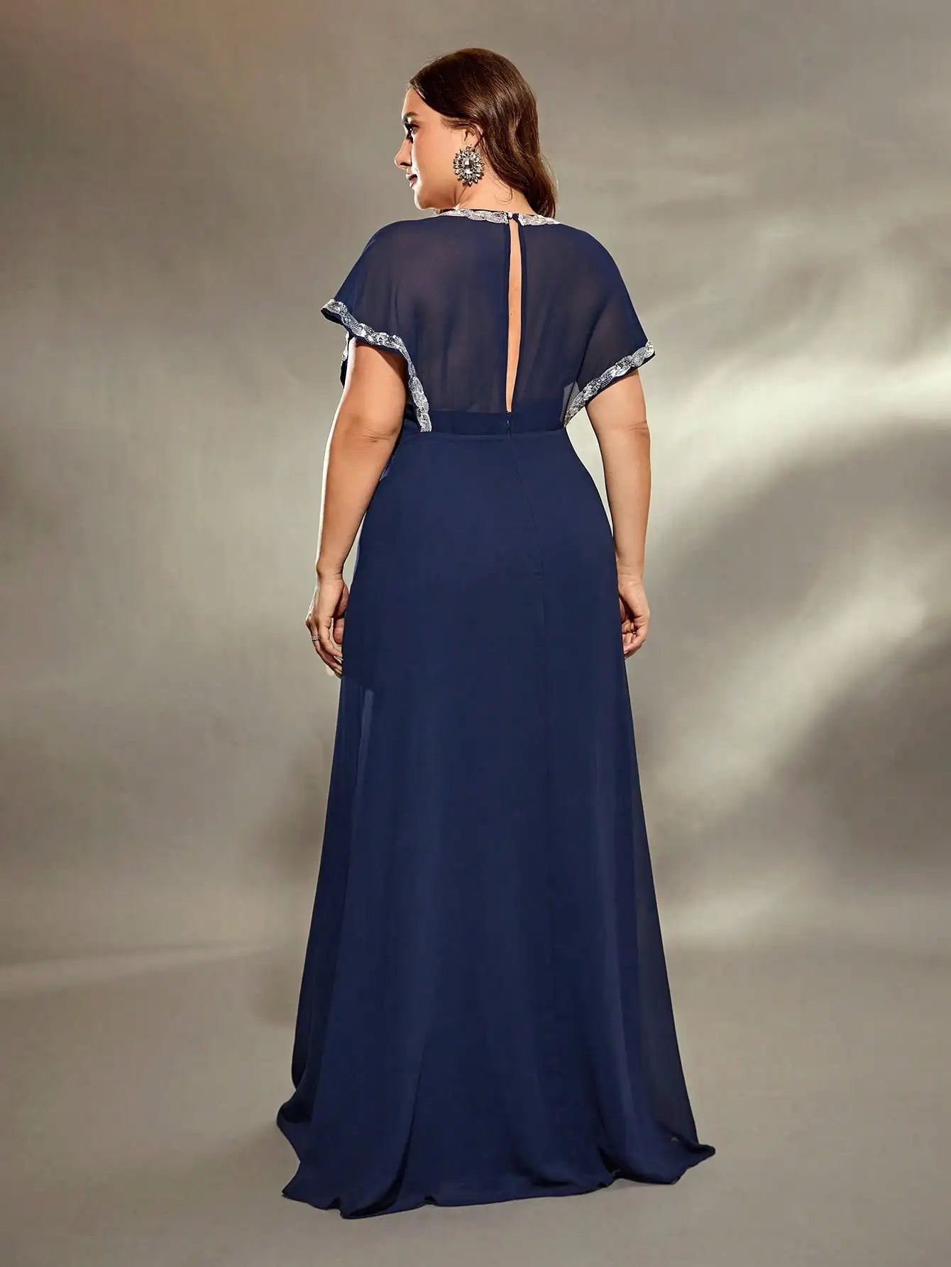 Woman wearing a navy blue evening gown with a sheer overlay on a gray background
