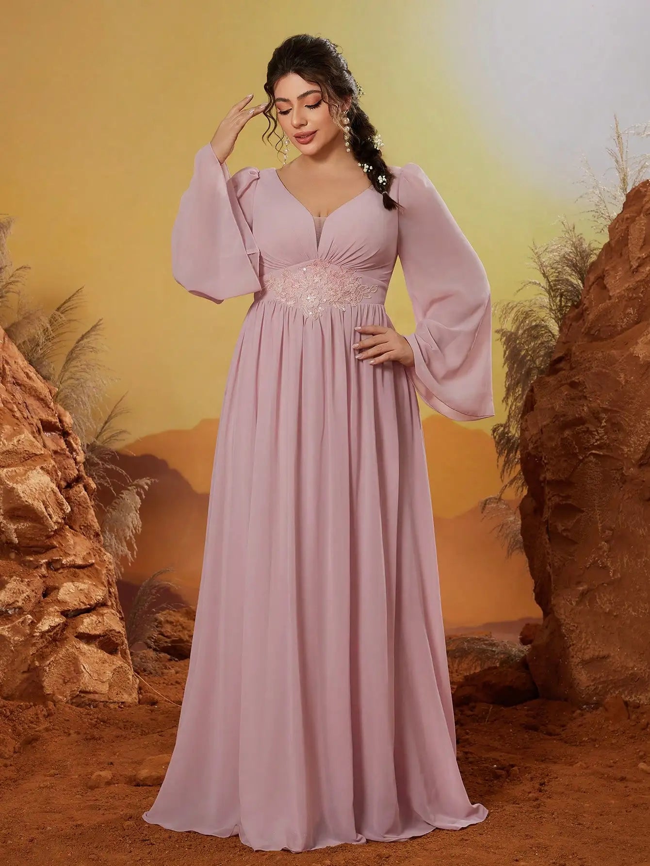 Woman in a pink dress standing in a desert-like setting with rocks and a yellow sky.