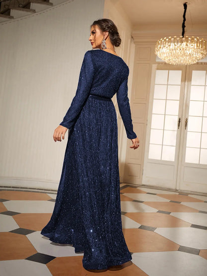 Woman in a long blue dress standing in an elegant room with a chandelier.