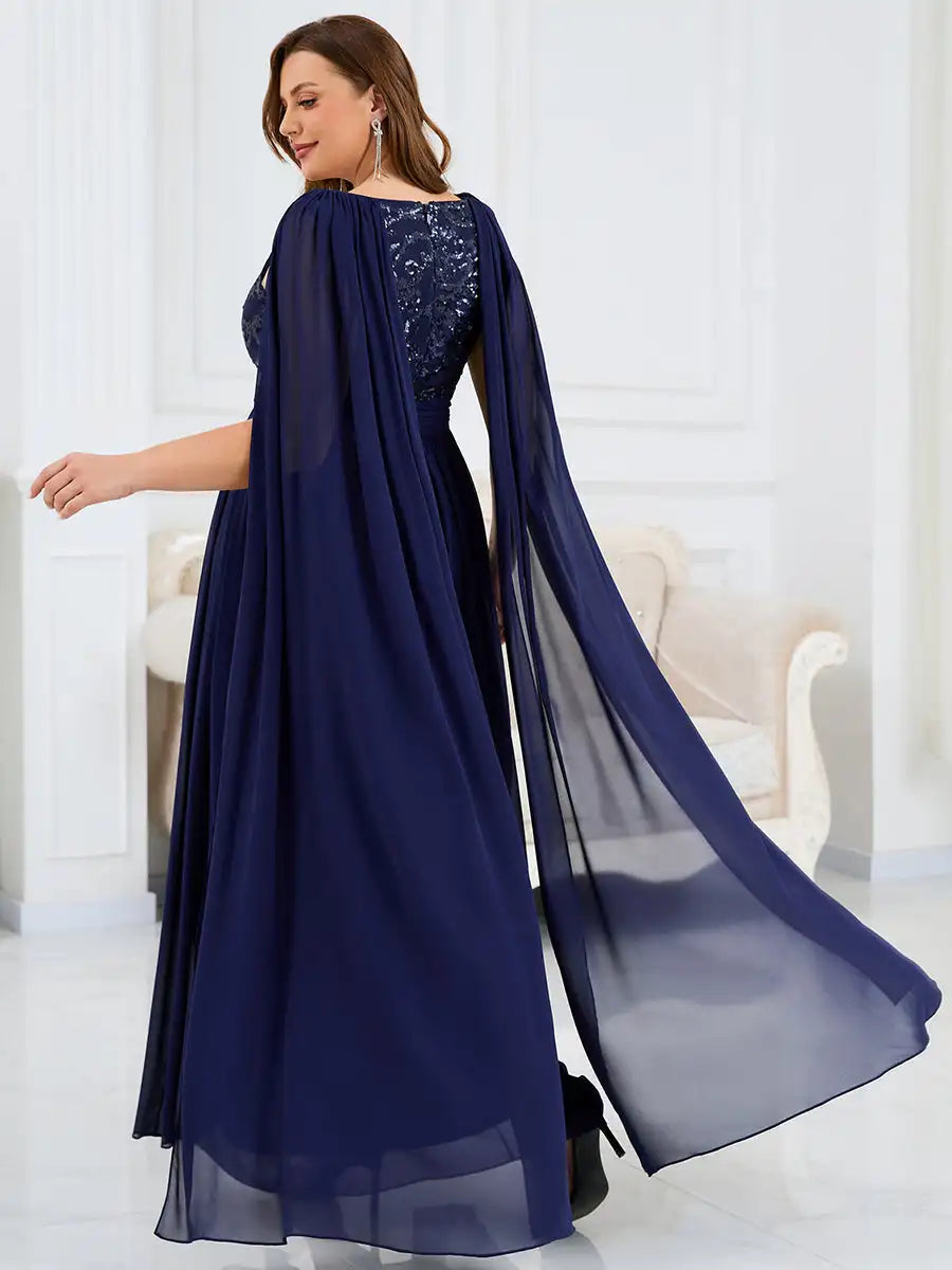 Woman wearing a long navy blue dress with a sheer overlay in a white room.