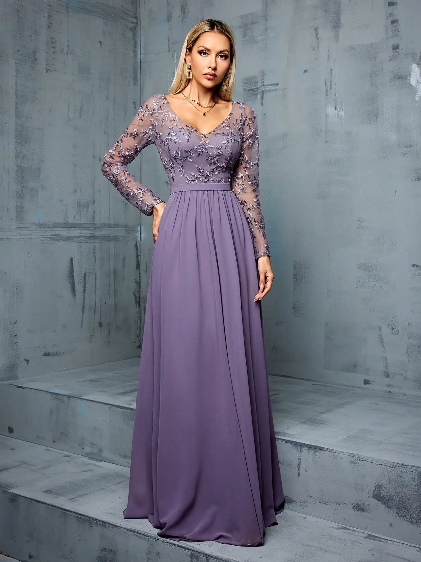 Woman wearing a long purple dress with lace sleeves against a gray concrete background
