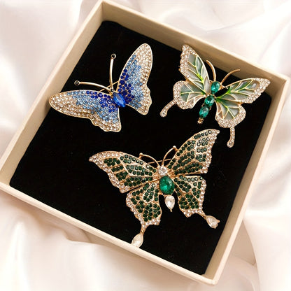 Three butterfly-shaped brooches with gemstones in a box on a white fabric background