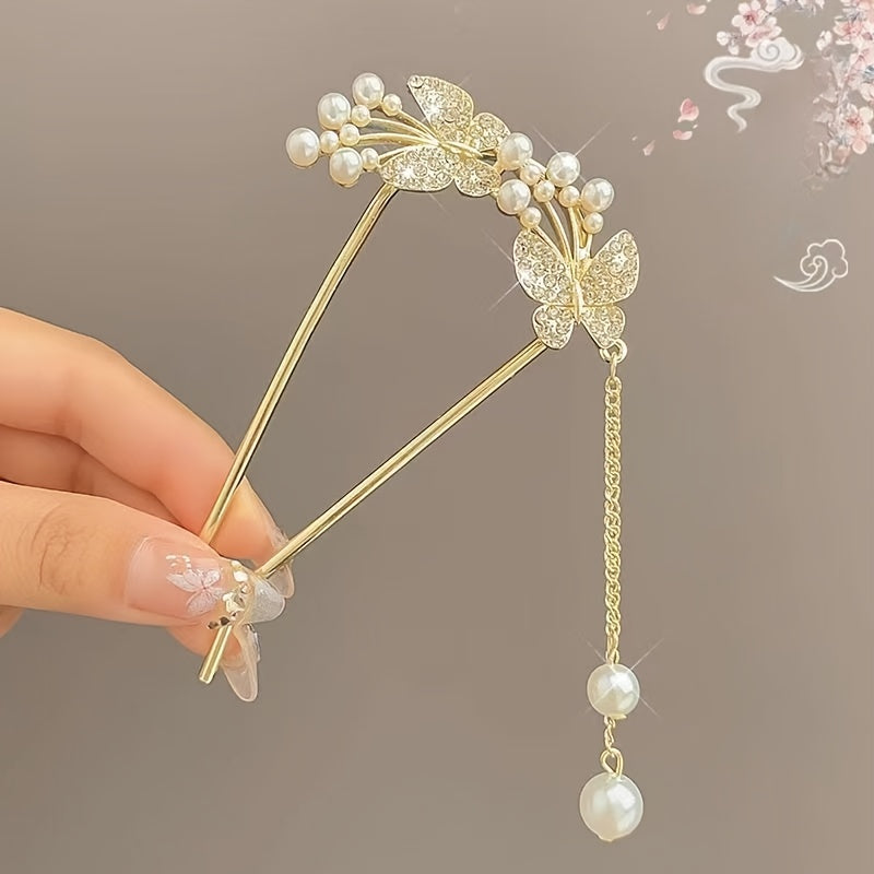 Gold hairpin with butterfly and pearl details held by a hand against a neutral background
